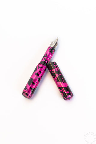 Pink fountain pen with black speckle pattern and metal nib, angled with cap shown