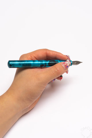 Teal anodized aluminum fountain pen held in hand, pointed nib visible