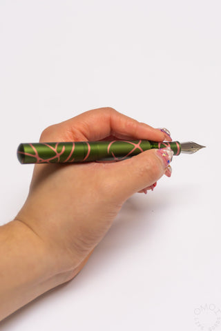 Pocket 6 fountain pen held in hand, green salmon splash with exposed pointed nib