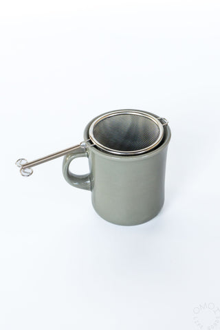 Stainless steel tea strainer with mesh basket and handle resting on mug