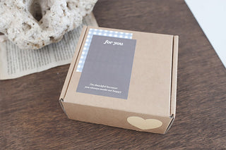 Sticker pack box in kraft paper with a heart cutout window on a wooden surface