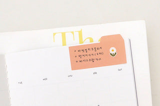 Planner calendar grid with orange tabbed sticky note and small printed label graphic
