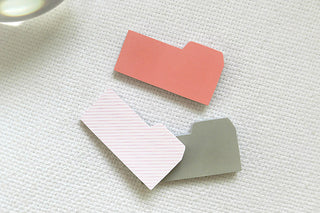 Tabbed sticky memo notes: orange, pink striped, and sage green tabs on fabric