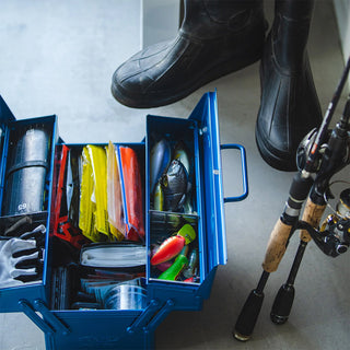 Blue cantilever toolbox open beside fishing gear and boots for storage use.
