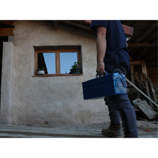Blue cantilever toolbox carried in hand outside near a building entry.