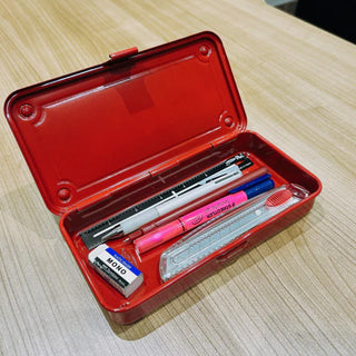 Red trunk toolbox open on a wood surface, with pens and stationery inside.
