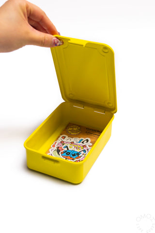 Yellow storage box with open lid, hand lifting hinged cover, compact rectangular shape.