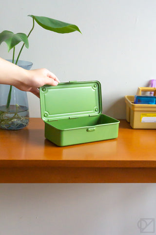 Green stackable storage box with lid open; person holds the hinged lid