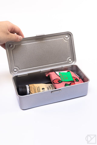 Silver-gray stackable storage box open with lid lifted by hand, containing supplies.