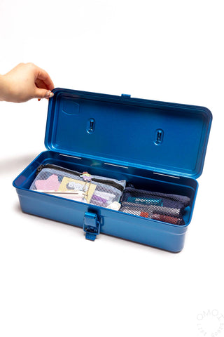 Blue trunk-shaped toolbox open, showing organizer with fabric pouches; hand holding lid
