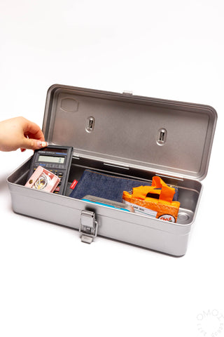 Silver trunk-shaped toolbox open; hand places a tool in the left compartment