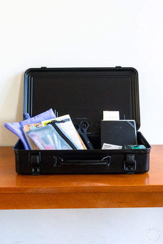 Black trunk toolbox open, holding files, scissors, and notebooks