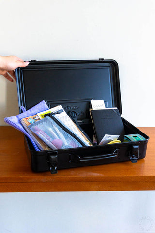 Black trunk toolbox open with hand lifting lid, stationery and cases inside