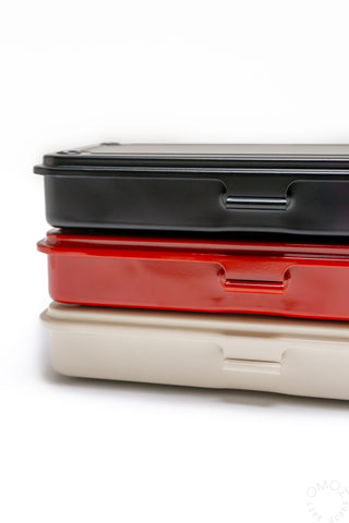 Stacked trunk-shaped toolbox lids: black top and off-white base with side slots.