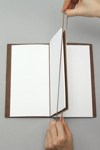 Hands installing connecting rubber bands on an open notebook with white refill sheets