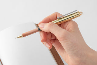 Wooden-shaft ballpoint pen with brass replacement tip, held in hand
