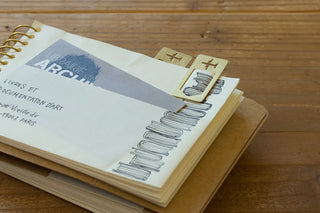 Brass airplane clips attached to notebook pages, two clips visible on wooden surface
