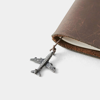 Pewter airplane charm attached to cord on brown leather cover edge.