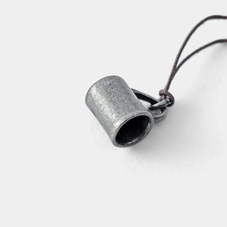 Pewter mug charm on cord, textured metal cylinder with stamped lettering.