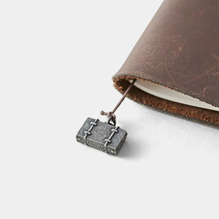 Pewter trunk charm on cord attached to brown leather notebook edge