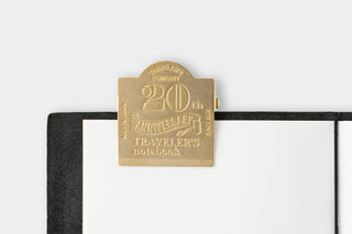 Gold 20th anniversary metal tag attached to a black notebook cover