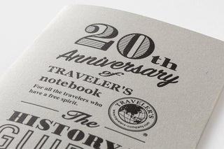 Close-up of white insert text: “20th Anniversary,” “TRAVELER’S notebook,” and “HISTORY GUIDE”