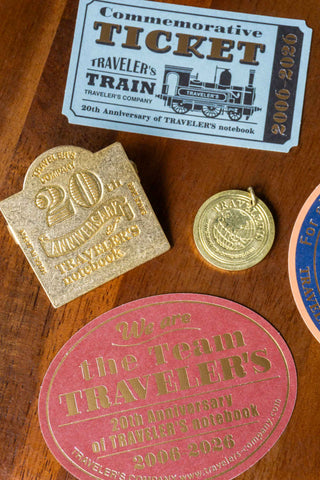 Wood surface with gold and pink anniversary seals and a “ticket” travel card