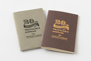 Two 20th anniversary notebook covers, one light and one dark, with gold logo