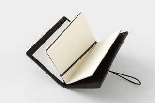 Black card-size notebook opened, showing cream pages and black spine strap.