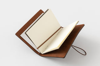 Brown leather card notebook opened, with cream pages and elastic closure strap.
