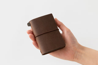 Hand holding brown card-size notebook cover with elastic band and button clasp