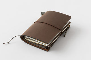 Brown leather card notebook closed with elastic strap, cords, and metal hardware.