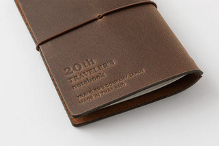 Close-up of brown leather notebook cover with embossed logo and stitched edge.