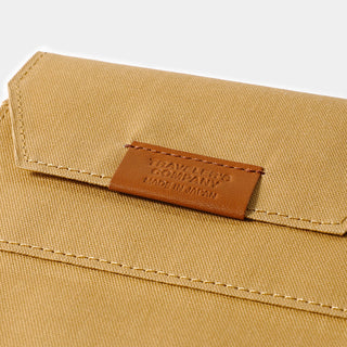 Brown leather brand label on beige cotton passport zipper case, with edge stitching.
