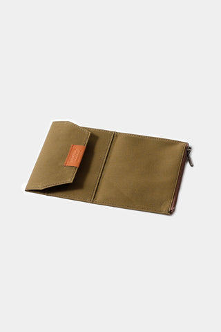 Olive passport-size zipper case with orange logo patch and metal zipper pull, angled view