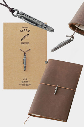 Pewter pen charm on dark cord attached to brown leather notebook cover with card