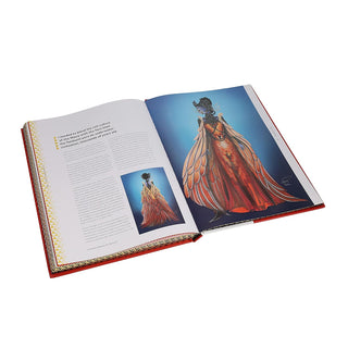 Open art book showing detailed costume illustration on blue page and adjacent text page