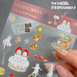 Hand holding clear gold-foil snack stickers on a windowed sheet with cute desserts
