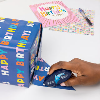 Hand applying MONO Air glue tape along a paper gift wrap edge