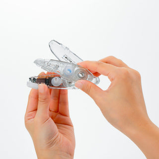Clear correction tape applicator with blue stripe, held by two hands