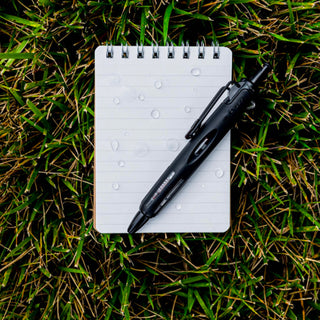 AirPress ballpoint pen on a notebook on grass, black pen with clip visible