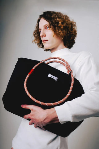 Person holding a black sling bag with a circular rope loop strap