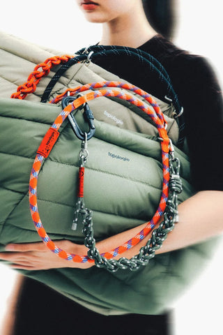 Model carrying a green bag with an orange-blue rope loop strap and silver hooks