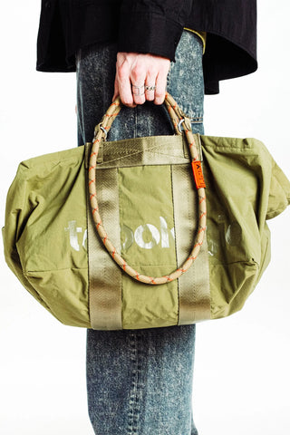 Woven rope loop strap with dark gray/black pattern and orange tag, on green tote
