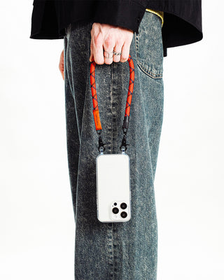 Red and black speckled wrist strap with phone clip, worn on denim