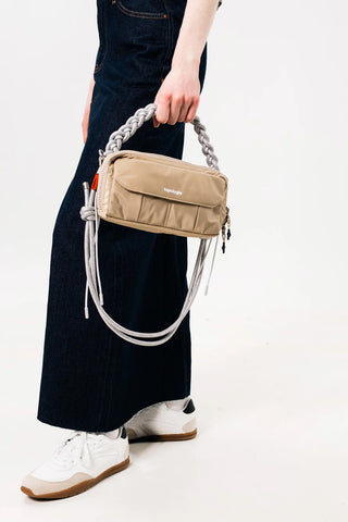 Light grey braided rope strap with metal rings and long tie cords on beige shoulder bag