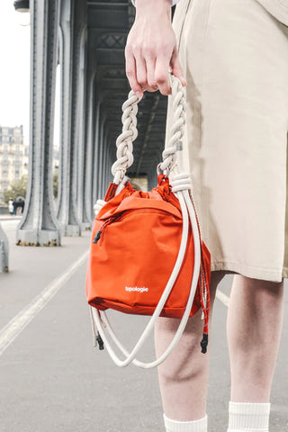 White braided rope handles with metal rings on orange mini drawstring bag