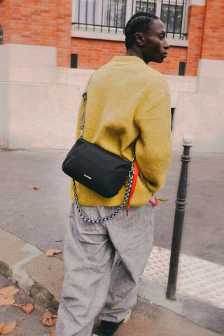 Black crossbody bottle sling bag worn at the side with blue strap accent