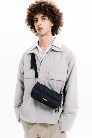 Black crossbody bottle sacoche with adjustable strap, worn over shirt, Topologie logo