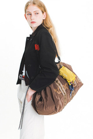 Mustard yellow mini bottle pouch worn crossbody with adjustable strap and drawstring.